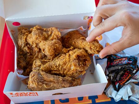 Womans hand grabbing piece of Popeyes Louisiana Chicken from dinner box in restaurantのeditorial素材