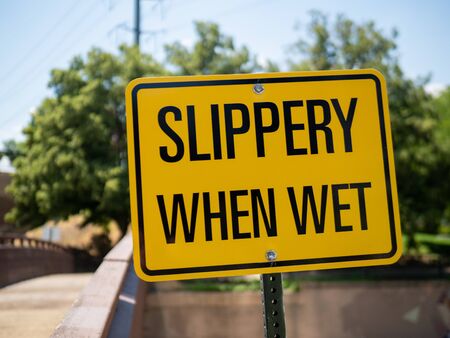 Slippery when wet yellow sign posting outdoors in front of bridgeの写真素材