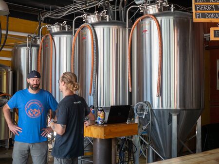 Two men talking in front of fermentation tanks at a breweryのeditorial素材
