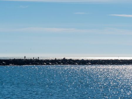People walking along rock seawall walkway in tourist beach areaの写真素材