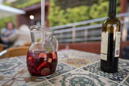 Pitcher of red sangria sitting next to red wine bottle on table at restaurantの写真素材