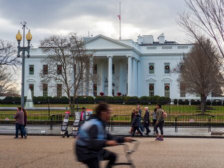 Man on bike races past White House lawn on overcast dayのeditorial素材