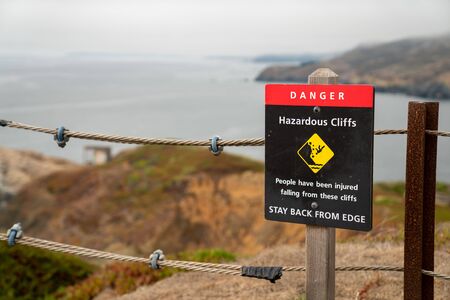 Danger hazardous cliffs stay back from edge sign on rope safety boundary warning visitors on hiking pathの写真素材