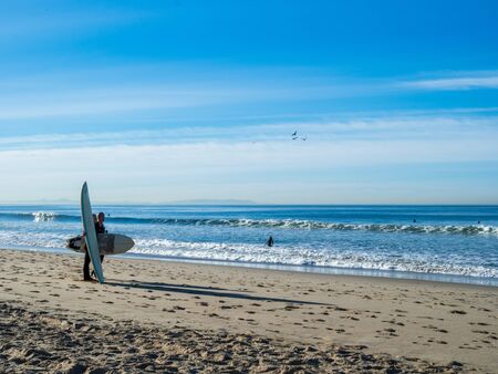 Man and woman holding surfboards on beach looking out to the oceanの写真素材
