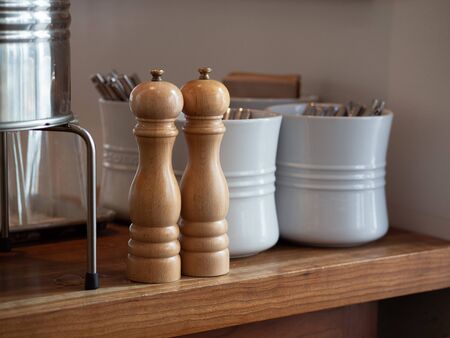 Wooden hand crank salt and pepper shaker on table with utensils in some ceramic potsの写真素材