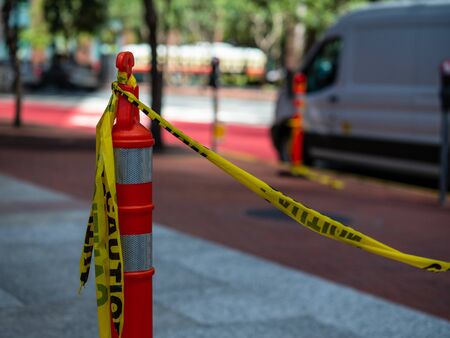 Yellow caution tape tied to orange safety cone on sidewalk with a van in backgroundの写真素材