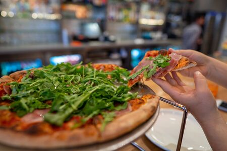 Woman grabbing slice of pizza with some arugula greens on topの写真素材