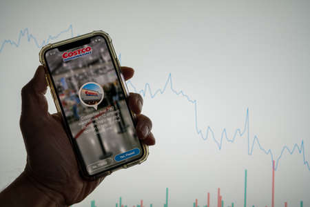 Costco mobile app iPhone in front of white stock market chart with graph going down in valueのeditorial素材