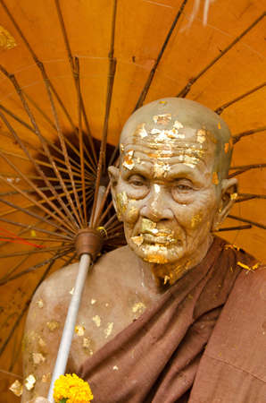 An old man made of clay holding an umbrella with gold on his faceの写真素材