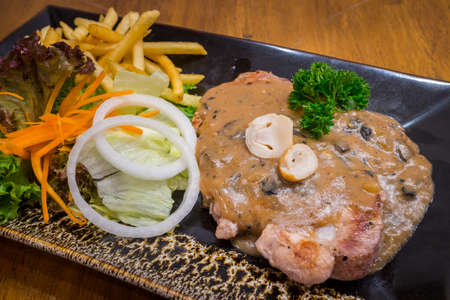 Healthy pork steak with mushroom sauce & salad in a black dish on wood table background for ready to serve.の写真素材