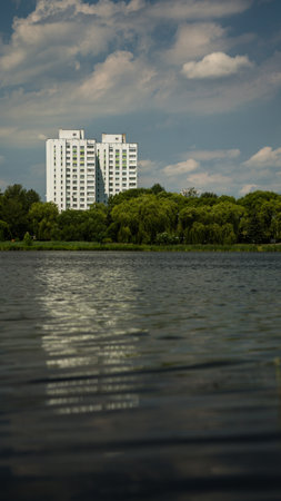 Two houses, multi-storey buildings, thick trees in front of them, and a large pondの写真素材