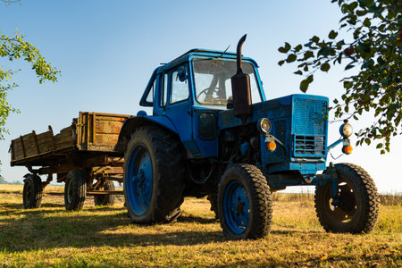 A blue, old tractor with a trailer stands near a field in the village. Morningの写真素材