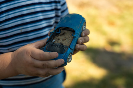 A child holds a toy car in his hand, filling it with sand. A toy in the hands