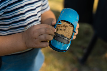 A child holds a toy car in his hand, filling it with sand.の写真素材