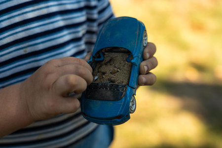 A child holds a toy car in his hand, filling it with sand. A toy in the hands