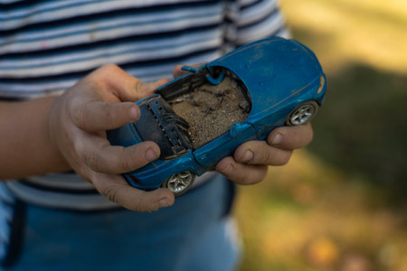 A child holds a toy car in his hand, filling it with sand.の写真素材