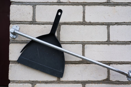 A plastic, black dustpan was stuck between the railing and the wall of the house. Brick wall background. High quality photoの写真素材