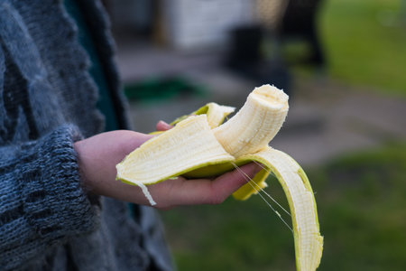 A bitten-off banana. The girl holds a banana in her hand. A girl in a sweater with a banana in her hand. High quality photoの写真素材
