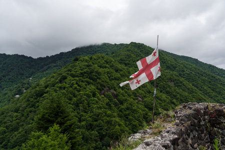 The flag of Georgia on the wall of the fortress of Gvara, on the background of the mountain. High...