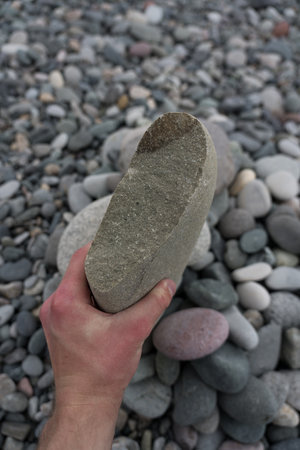 A large flat broken stone in the hands of a man on the background of a stone beach. High quality photoの写真素材