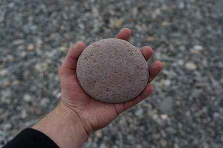 A round stone in the hand of a man on the background of the stone beach of Batumi. High quality...