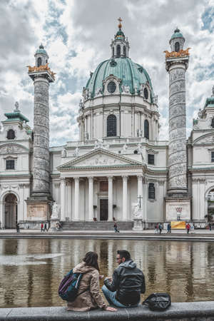 Vienna, Austria - April 28, 2019: Lovers sit by the fountain in front of Karlskirch durring sunny dayのeditorial素材