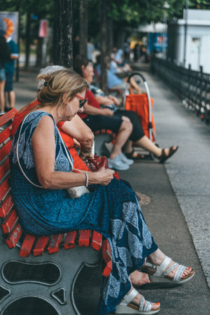 Lugano, Switzerland - August4, 2019: Tourists rest on red bench facing Lugano Lake in summer timeのeditorial素材