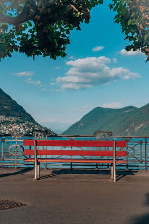 Red bench by lugano lake with view of monte bre and clouds in blue skyの写真素材