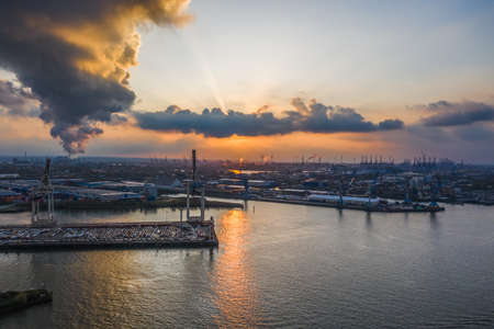 Sunset with dramatic clouds at port of Hamburg with heavy-lifting crane by the seaの写真素材