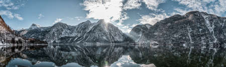 Panoramic view of snowy Hallstatt village houses by lake with a ray of sunshine in winterの写真素材