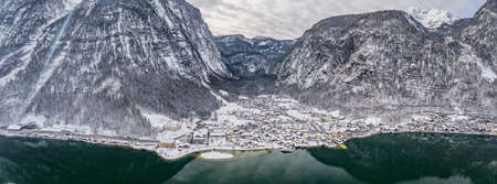 Aerial panoramic drone shot of Lahn village at foot of snow mountain by lake Hallstatt in Austria during overcast winterの写真素材