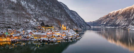 Panoramic aerial drone view of Hallstatt village with lights on by lake during sunset hour in winter timeの写真素材
