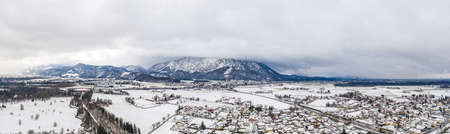 Panoramic aerial view of Austrian mountain half in fog with Anif snowy village in outskirt in the foregroundの写真素材