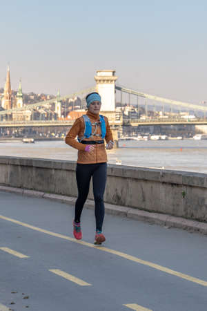 Budapest, Hungary - Feb 9, 2020: Female jogger by Danube river in the afternoon with Liberty bridge in backgroundのeditorial素材