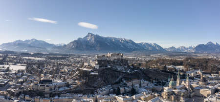 Panoramic aerial drone view of snowy Hohensalzburg fortress with view of Unesberg mountain in winter morningの写真素材