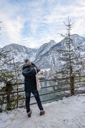 Feb 6, 2020 - Hallstatt, Austria: Female tourist in black down jacket take photo of snowy church in Hallstatt in winterのeditorial素材