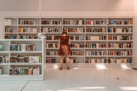 Stuttgart, Germany - Aug 1, 2020 - Woman with mask reading book at Stadtbibliothek library with sun...