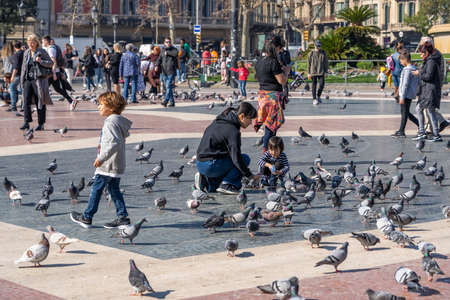 Barcelona, Spain - Feb 24, 2020: Pedestrians feed pigeons on Plaza de Catalunya on sunny afternoon in winterのeditorial素材