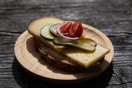 Delicious fresh bread with hay milk cheese, cucumber, tomatoes and red onions on wooden plateの写真素材