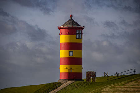 The yellow and red lighthouse of Pilsum with dark clouds in the backgroundの写真素材