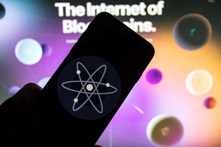 Rheinbach, Germany 15 February 2022, The logo of the cryptocurrency "Cosmos" on the display of a smartphone in front of the website (focus on the logo)のeditorial素材