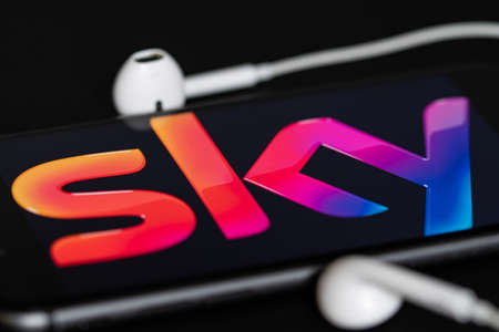 Rheinbach, Germany April 28, 2022, The brand logo of the pay TV provider "Sky" on the display of a smartphone with headphones (focus on the brand logo)のeditorial素材