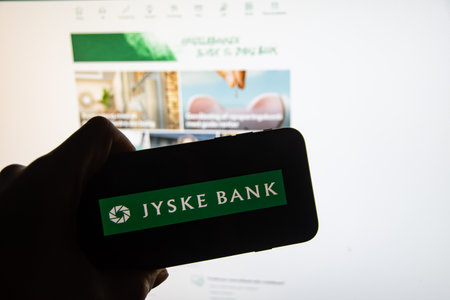 Rheinbach, Germany 26 February 2023, The brand logo of the Danish financial service provider "Jyske Bank" on the display of a smartphone in front of the website (focus on the braのeditorial素材