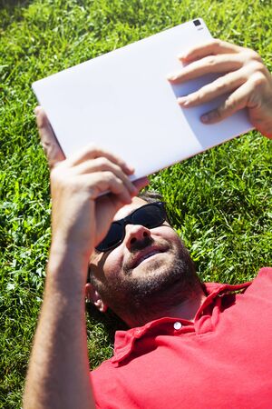 Man reading news in a tablet while lying on the grass.の写真素材