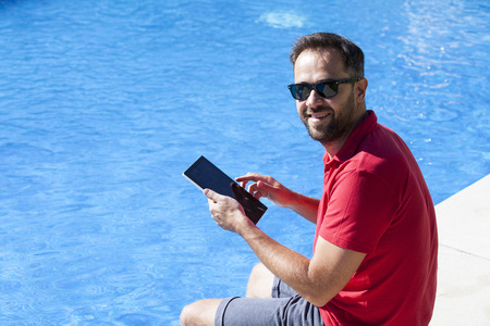 Man using a tablet at the poolside.の写真素材