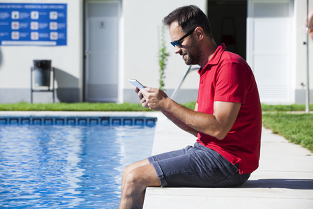 Man reading a tablet sitting at the poolside.の写真素材