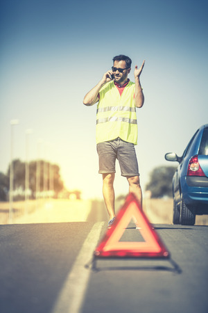 Angry man discussing with assistance company by phone after car breakdown.の写真素材