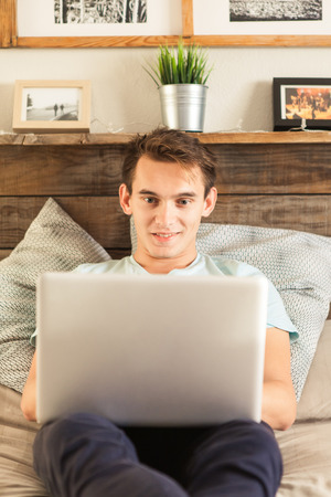 Smiling young man in front of a laptop while lying at home.の写真素材