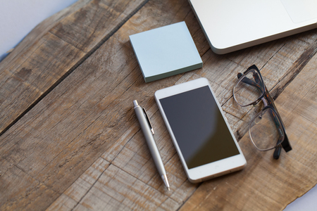 Smartphone, glasses, pen and computer over wooden table desk.の写真素材