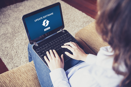 Woman with a laptop on her knees at home. Update software notification in the screen.の写真素材